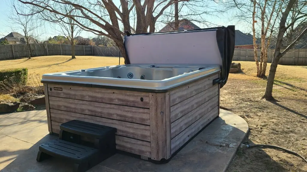 Outdoor hot tub with wooden siding and cover in a backyard.