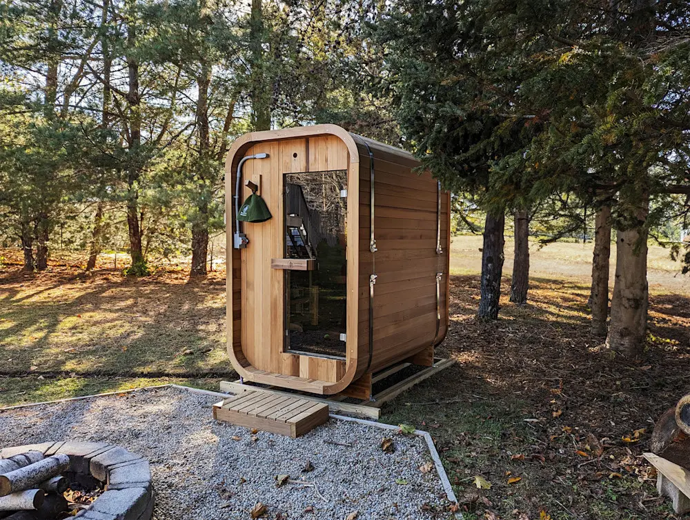 A modern wooden sauna cabin nestled in a forest clearing.
