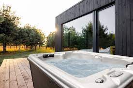 Outdoor hot tub with a sunset view beside modern house windows.