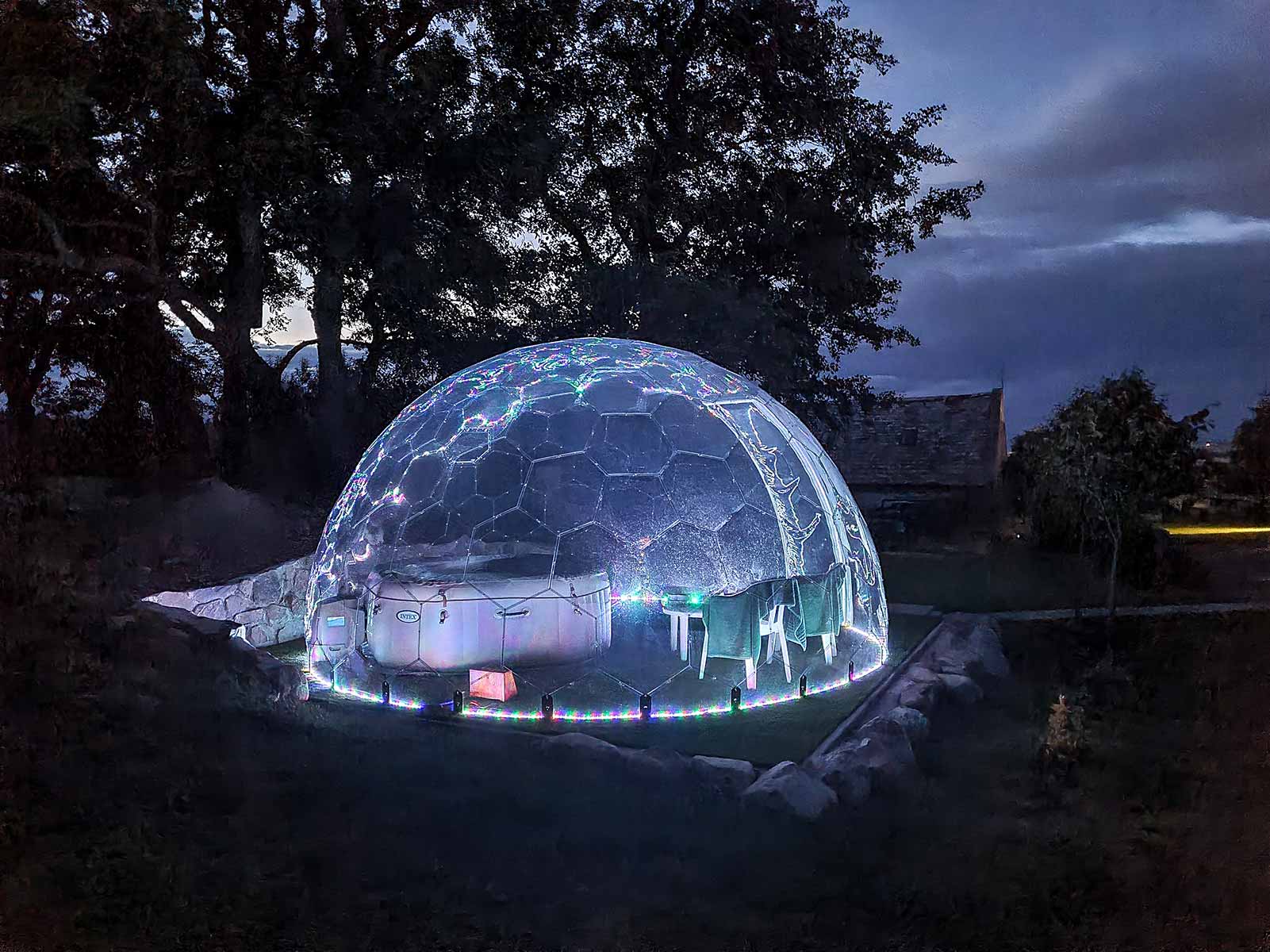 Illuminated transparent dome tent glowing at night in a natural setting.