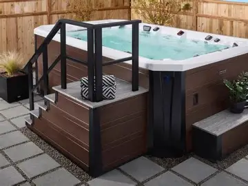 Modern outdoor hot tub with wooden stairs and black railing.